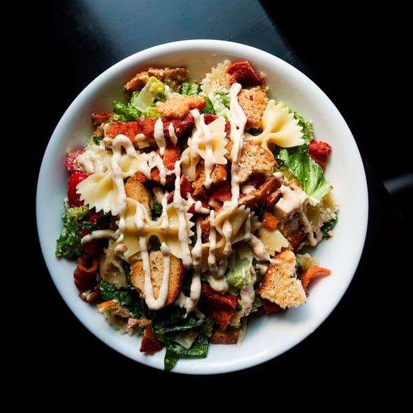 Nunzi's Italian salad with farfalle pasta, bacon, croutons, and creamy dressing in a white bowl.