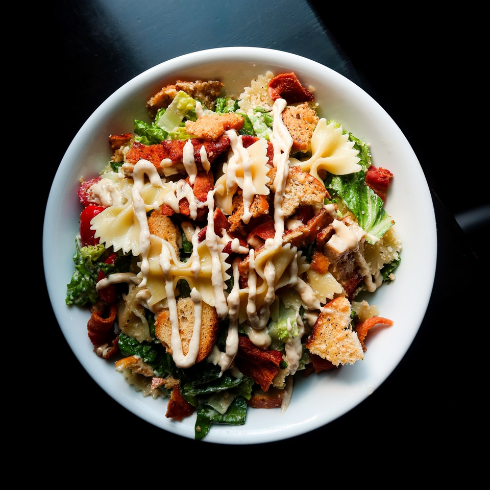 Nunzi's Italian salad with farfalle pasta, bacon, croutons, and creamy dressing in a white bowl.