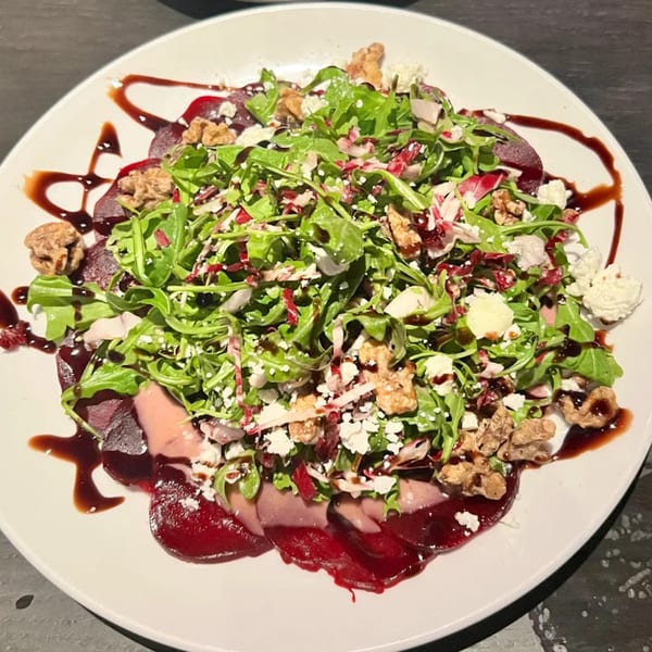 Nunzi's beet carpaccio with arugula, walnuts, goat cheese, and balsamic glaze on a white plate.