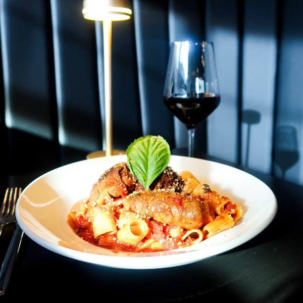 Nunzi's rigatoni with meatballs and sausage, garnished with basil, beside a glass of red wine.