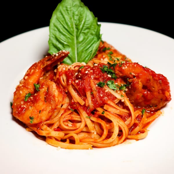 Nunzi's shrimp linguine with red sauce, parmesan, and basil on a white plate.