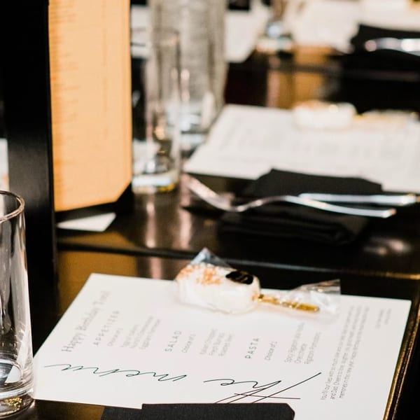 A Nunzi's menu with a cake pop and empty glass on a dark table, ready for a meal.