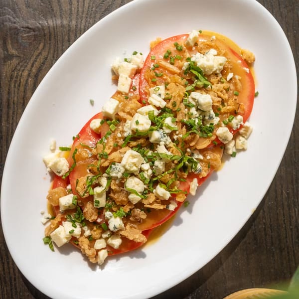 Nunzi's Italian tomato salad with blue cheese, crispy onions, and chives on a white plate.