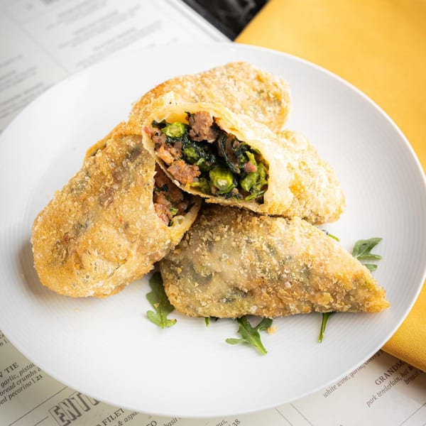 Four crispy Italian egg rolls, one cut open to reveal a savory filling of meat and greens.