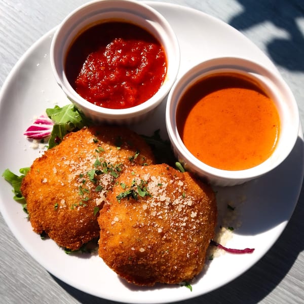 Two golden-brown fried arancini balls with marinara and vodka sauce on a white plate.