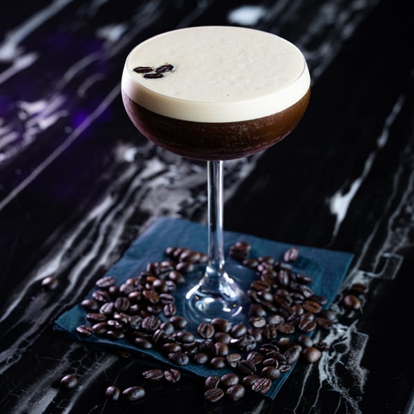 Nunzi's espresso martini with coffee beans on a dark marble table.