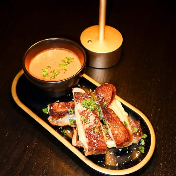 Nunzi's Italian dish with sliced meat, creamy sauce, and a side of soup on a black tray.