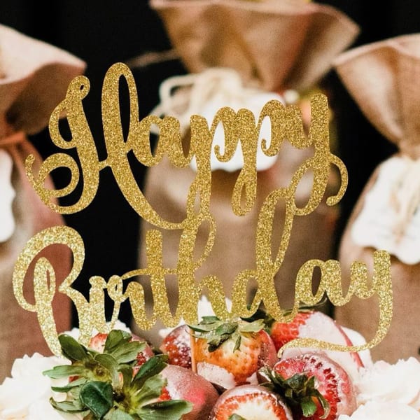 A "Happy Birthday" cake topper in gold glitter, with strawberries and whipped cream.
