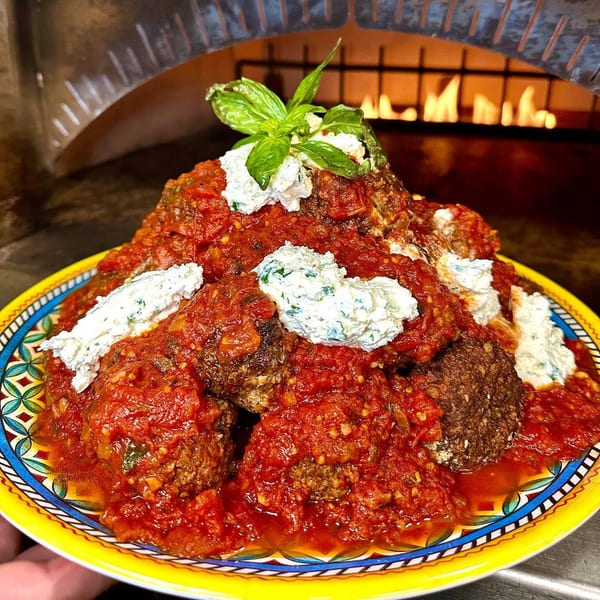 Nunzi's Italian meatballs with red sauce, ricotta, and basil, in front of a pizza oven.